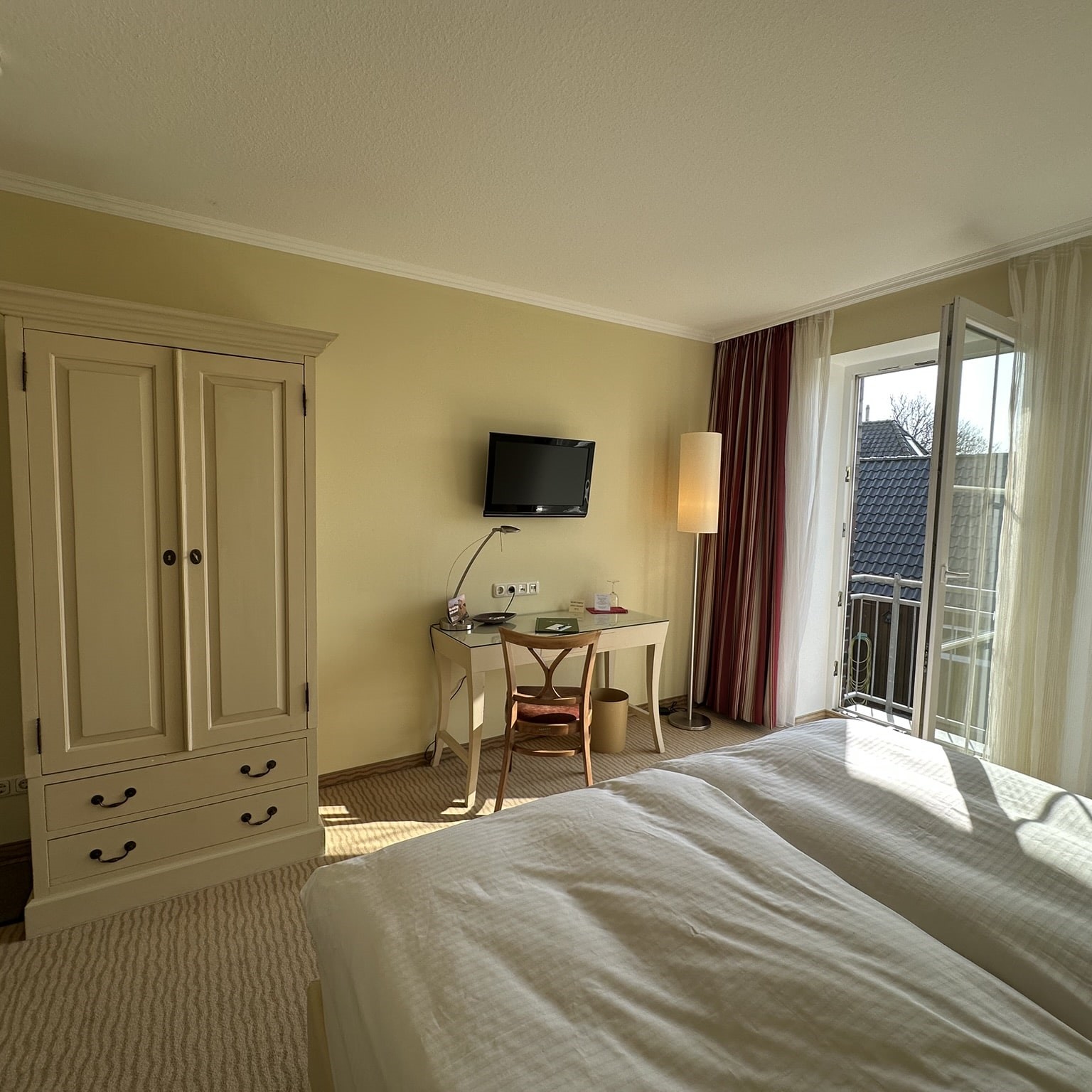 Hotelzimmer mit weißem Schrank, roten Vorhängen und offenem Fenster. 